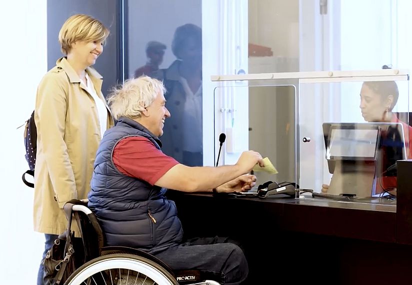 Besucher im Rollstuhl und Begleiterin kaufen Tickets am Ticketschalter des Deutschen Museum.