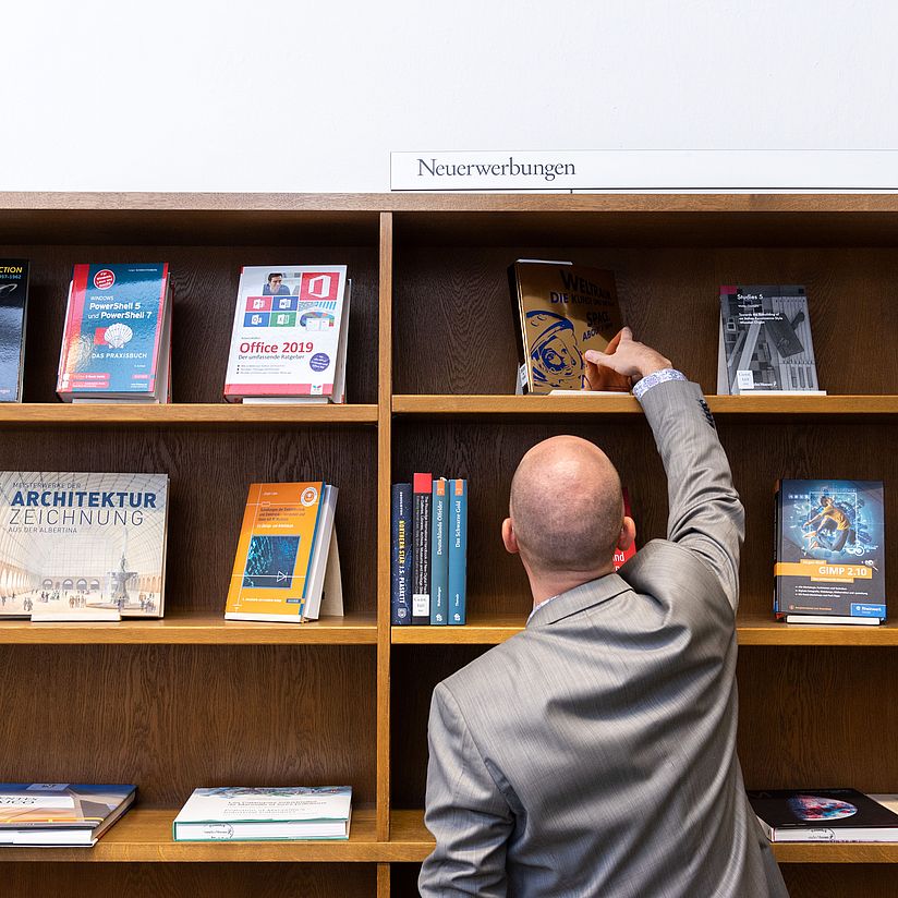 Neuerwerbungsregal Ein Nutzer nimmt ein Buch aus dem Neuerwerbungsregal.