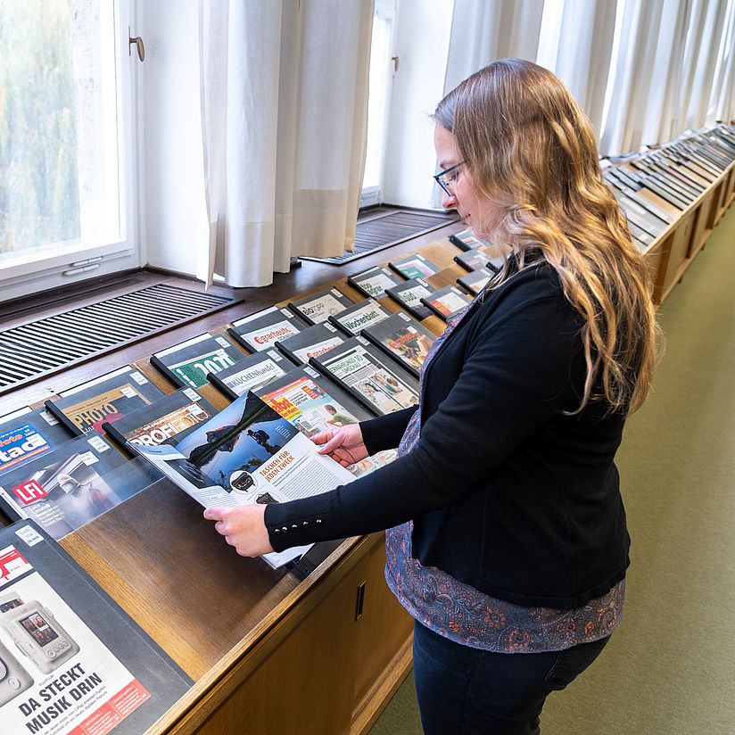 Blättern in der Zeitschriftenauslage im Lesesaal Benutzerin blättert in einer Zeitschrift im Lesesaal.